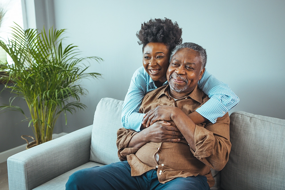 couple sitting on the couch, with a happy woman hugging her husband from behind